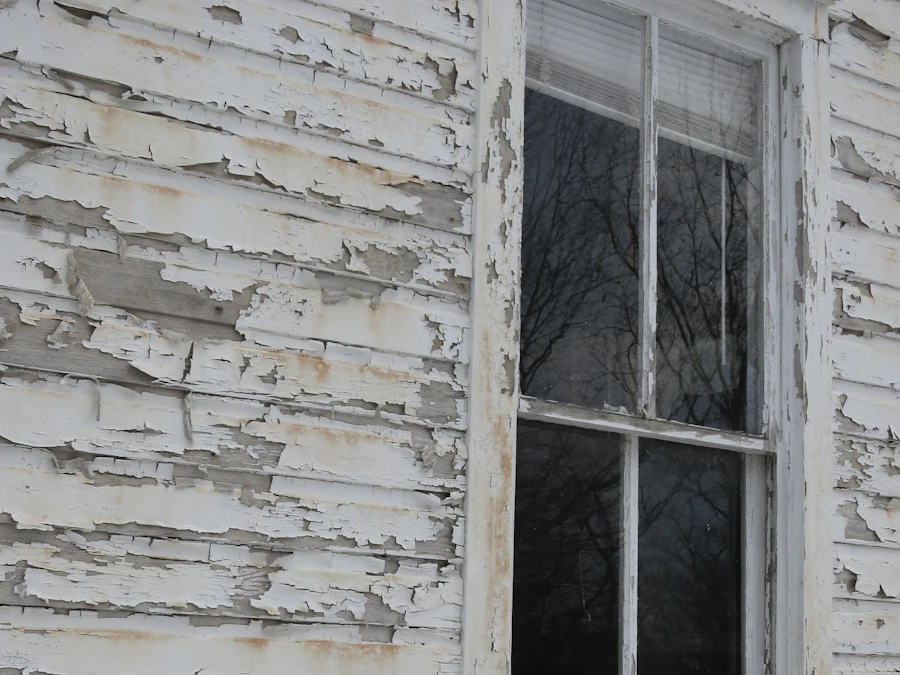 Before: weathered clapboard siding with paint peeling away around a window